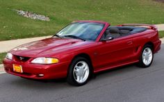 a red sports car is parked on the side of the road in front of some grass