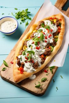 a long piece of bread with meat and sour cream on it sitting on a cutting board