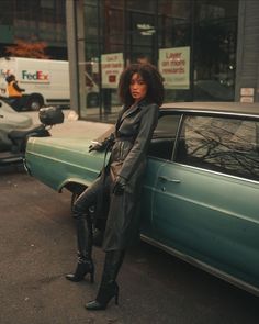 a woman leaning on the side of a car in front of a parked green car