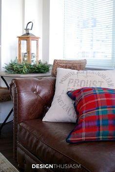 a brown leather couch with plaid pillows and christmas decorations on the table in the background