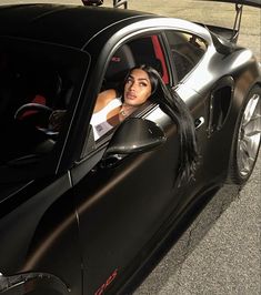 a woman sitting in the driver's seat of a black sports car