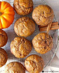 several muffins on a wire rack with cinnamon sticks and an orange pumpkin in the background