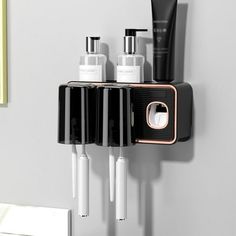 three toothbrushes and two tube holders on a wall with hairdryer in the corner