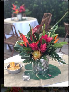 a table topped with a metal can filled with flowers and other items next to a bowl of chips