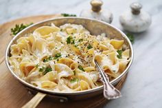 a silver bowl filled with pasta and parsley on top of a wooden cutting board