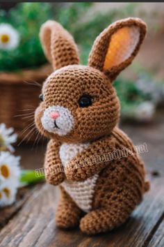 a crocheted bunny sitting on top of a wooden table next to daisies