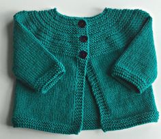 a green knitted cardigan with buttons on the front and back, sitting on a white surface