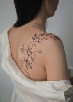 a woman wearing a white dress has a tattoo on her shoulder and is looking at the camera