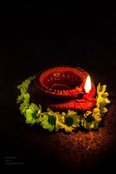 a lit candle sitting on top of a table next to green leaves and flowers in the dark