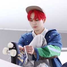 a young man with red hair is holding a skateboard and tying it to his shoe