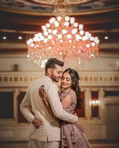 a man and woman standing next to each other in front of a chandelier