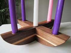 four candles are arranged in the center of a wooden stand with purple and white pillar tops