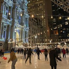 people skating on an ice rink at night in front of a large building with lit up windows