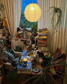 a cluttered living room with lots of plants and books on the table, in front of a large window