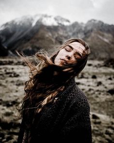 a woman with her hair blowing in the wind on top of a mountain, wearing a sweater