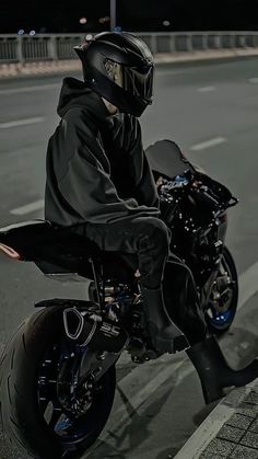 a man riding on the back of a black motorcycle down a street at night time