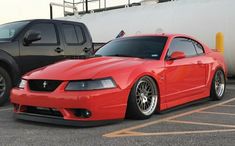 a red mustang parked in a parking lot next to a truck and another black one