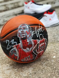 a basketball sitting on top of a stone floor next to another ball with an image of a man's face painted on it