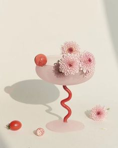 a pink vase with flowers on it and some strawberries next to it in front of a white background