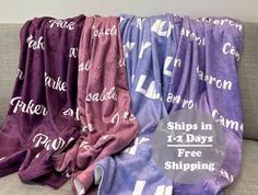 three purple and blue towels with white letters on them are sitting on a gray couch