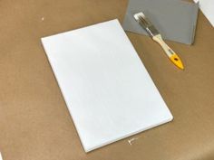 a white piece of paper with a yellow handled brush next to it on a table