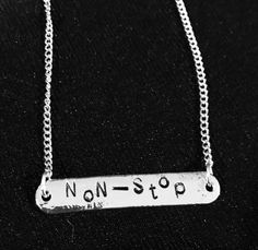 a silver necklace with the word non stop written in black and white ink on it