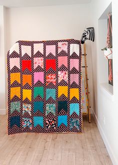 a colorful quilt hanging on the wall next to a ladder in a room with white walls