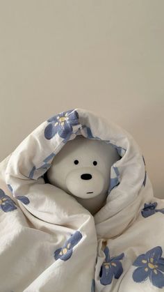 a white teddy bear wrapped in a blanket with blue flowers on it's head