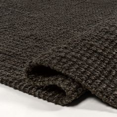 a close up view of a knitted blanket on a white surface with the fabric pulled back