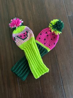 two knitted hats sitting on top of a wooden floor next to each other with pom poms