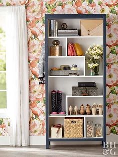 an open bookcase in front of a floral wallpaper