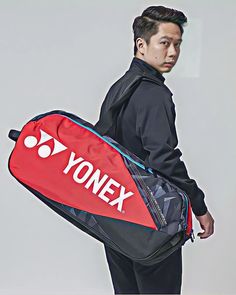 a man holding a red and black bag with yonex on the bottom side