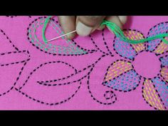 someone is stitching flowers on a piece of pink fabric with green thread and needles