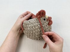 a person holding a small crocheted chicken in their left hand, on a white surface