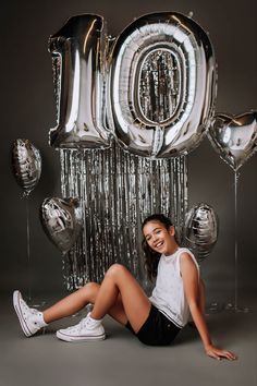 a woman sitting on the ground in front of balloons and streamers that spell out the number ten