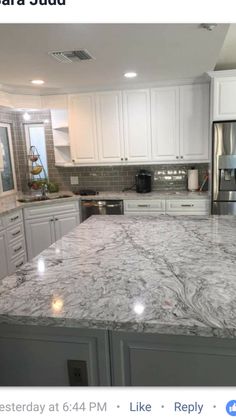 a kitchen with white cabinets and marble counter tops