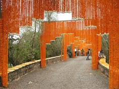 people are walking through an orange structure with chains hanging from it's sides and trees in the background