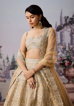 Elevate your bridal look with our stunning champagne lehenga, a must-have for your special day. This exquisite ensemble features intricate gold and silver embroidery that adds a touch of opulence. Heavily adorned with sequins, delicate pearlwork, and shimmering crystal stones, it promises to make you the center of attention as you celebrate in style. This lehenga perfectly balances elegance and glamour, ensuring you shine on your momentous occasion. Champagne Gold Lehenga, Ivory Gold Lehenga, Gold Embellished Semi-stitched Lehenga, Gold Semi-stitched Hand Embellished Lehenga, Golden Shimmer Lehenga, Gold Lehenga, Silk Organza, Champagne Gold, Indian Design