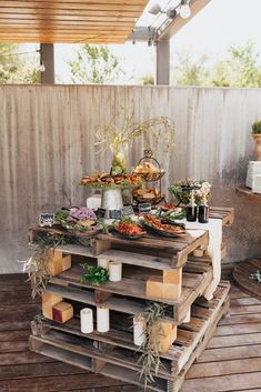 a wooden table topped with lots of food on top of a wooden floor next to a fence