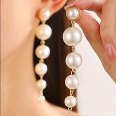 a close up of a person holding a pair of earrings with pearls attached to it