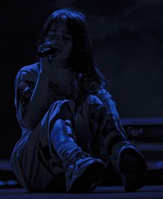 a woman sitting on the ground while holding a microphone in her hand and looking down