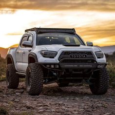 a white toyota truck parked on top of a dirt hill at sunset in the desert