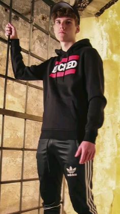 a young man is standing in front of a wall wearing adidas tracksuits