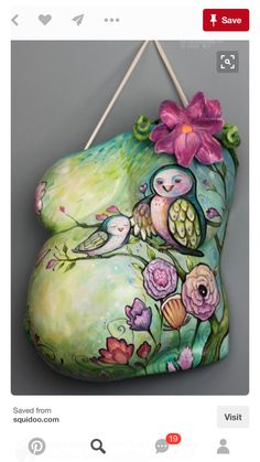 a painted rock hanging on a wall with flowers and two birds sitting on the branch