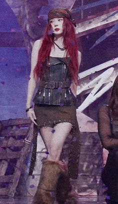 a woman with long red hair walking down a runway wearing a leather outfit and boots