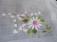 white flowers and green leaves are embroidered onto a gray linen tablecloth with pink trim