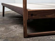 a wooden bed frame sitting on top of cement flooring next to a white wall