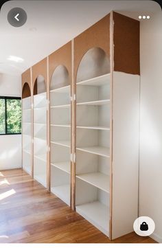 an empty room with white shelves and wood flooring on the walls, in front of a large window