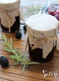 two jars filled with jam sitting on top of a wooden table next to blackberries