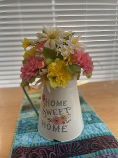 a white vase filled with flowers sitting on top of a table next to a window